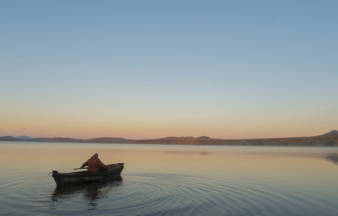 Hohe Winkel Ansicht des Mannes in Boot auf See gegen klaren Himmel während des Sonnenuntergangs, lizenzfreies Stockfoto