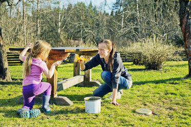 Mutter mit Tochter streichen Holztisch im Garten - FOLF03611