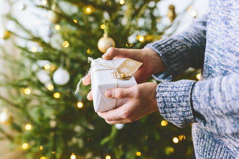 Mann hält Weihnachtsgeschenk gegen Weihnachtsbaum - FOLF03644