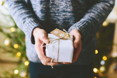 Mann hält Weihnachtsgeschenk gegen Weihnachtsbaum, lizenzfreies Stockfoto