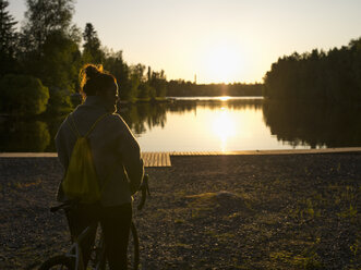 Silhouette einer am Fluss stehenden Frau bei Sonnenuntergang - FOLF03674
