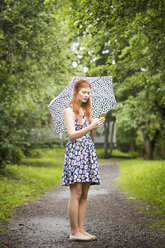 Frau in geblümtem Kleid steht mit Regenschirm im Park - FOLF03684