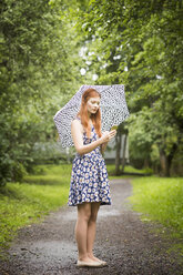 Woman wearing floral dress standing with umbrella in park - FOLF03684