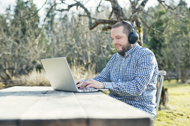 Mittlerer Erwachsener Mann benutzt Laptop im Garten - FOLF03842