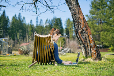 Mittlere erwachsene Frau liegt auf einer Sonnenliege im Garten und benutzt einen Laptop - FOLF03843