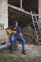 Junger Mann spielt Gitarre im Freien auf einem Bauernhof - AFVF00373