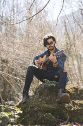 Junger Mann sitzt auf einem Felsen und spielt Gitarre - AFVF00376