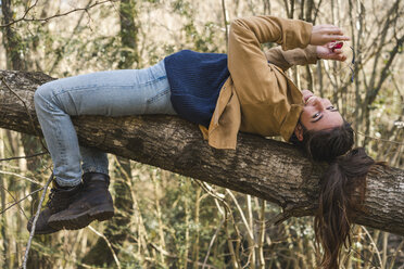 Happy young woman lying on a tree trunk in nature - AFVF00380