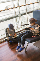 Zwei Jungen sitzen und spielen mit Tablets im Wartebereich des Flughafens Arlanda - FOLF03906