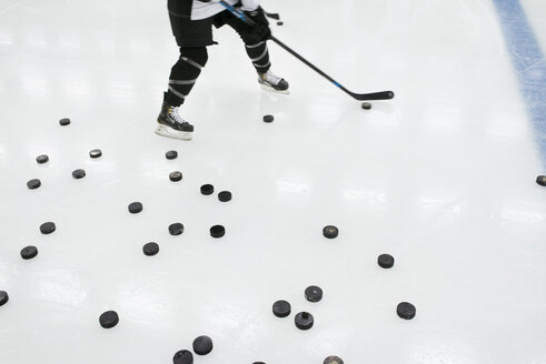 Junger Eishockeyspieler mit einer großen Anzahl von Pucks auf der Eisbahn - FOLF03970