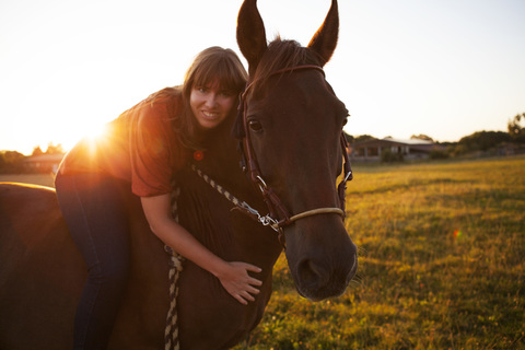 Portrait of smiling woman on horse at sunset stock photo