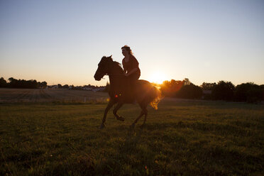 Woman horse-riding on field at sunset - FAF00083