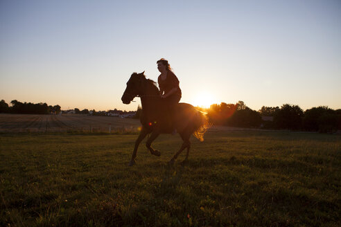 Frau reitet bei Sonnenuntergang auf einem Feld - FAF00083