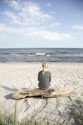 Reife Frau sitzt auf Treibholz und schaut aufs Meer - FOLF04209