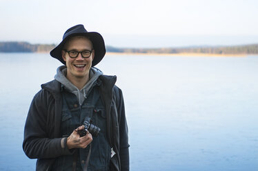 Smiling man holding digital camera and lake in background - FOLF04255