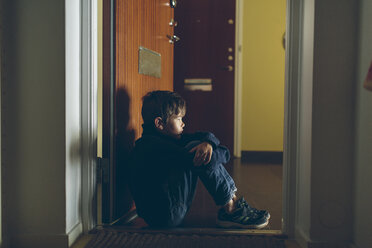Boy sitting on floor next to door - FOLF04283