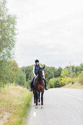 Mittlere erwachsene Frau reitet auf Pferd auf Straße durch Wald - FOLF04313