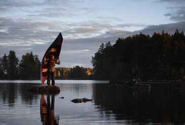 Man standing on stone in lake holding canoe - FOLF04326