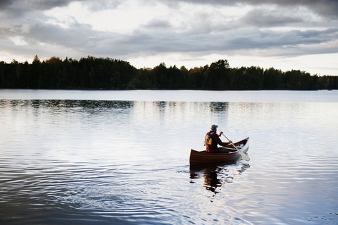 Mann paddelt mit Kanu auf einem See, lizenzfreies Stockfoto