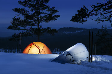 Beleuchtete Zelte auf Schnee mit bewaldeten Bergen im Hintergrund - FOLF04338