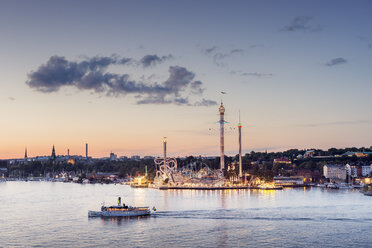 Beleuchteter Vergnügungspark Grona Lund in Stockholm bei Sonnenuntergang, über das Wasser gesehen, mit vorbeifahrendem Schiff - FOLF04390
