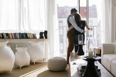 Umarmung eines Paares am Fenster im Wohnzimmer - FOLF04570