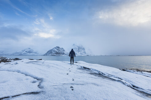 Mann steht im Schnee und schaut aufs Meer hinaus - FOLF04762