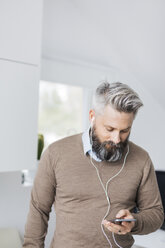 Mann mit Kopfhörern, der sein Mobiltelefon abhört - FOLF04766