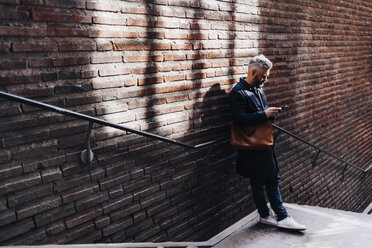 Mann neben einer Ziegelmauer mit Smartphone - FOLF04848