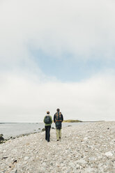 Rückansicht eines Paares, das an der felsigen Küste spazieren geht - FOLF04869