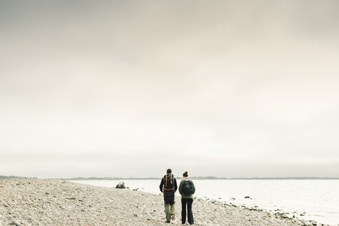 Rückansicht eines Paares, das an der felsigen Küste spazieren geht - FOLF04873