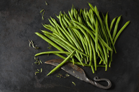 Needle beans, sayory and an old knife on dark metal stock photo