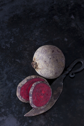 Ganze und geschnittene Rote Bete und ein altes Messer auf dunklem Metall, lizenzfreies Stockfoto