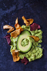 Guacamole, eine Scheibe Avocado und Gemüsechips auf dunklem Grund - CSF29030