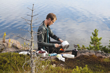 Junger Mann beim Kochen am Flussufer in High Coast, Schweden - FOLF05171