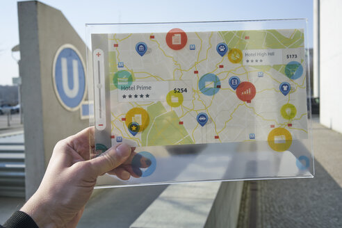 Hand hält futuristisches Gerät mit digitalen Symbolen und Karte in der Stadt - FMKF05018