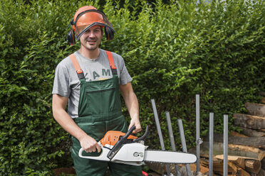 Portrait of smiling man wearing protective clothes holding motor saw - PAF01787