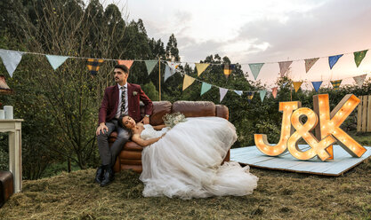 Bride lying over sofa with groom in the field - DAPF00926