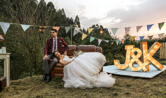 Braut auf Sofa liegend mit Bräutigam auf dem Feld - DAPF00926