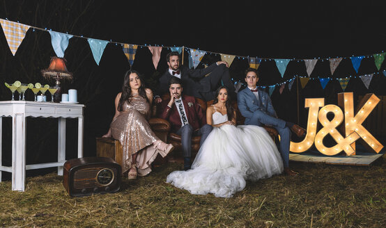 Porträt eines Hochzeitspaares mit Freunden auf dem Sofa auf einer nächtlichen Feldparty - DAPF00931