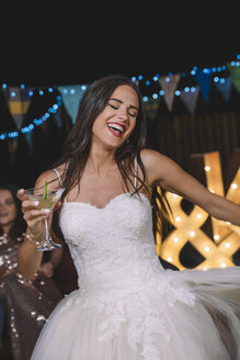 Happy bride laughing and dancing while holding cocktail on an outdoor night party - DAPF00935