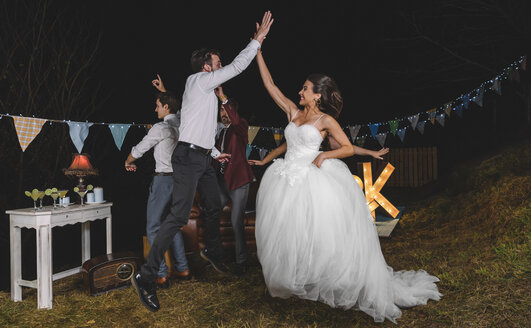 Glückliche Braut springt und gibt high five mit jungen Mann auf einer Nacht Feld Partei mit Freunden - DAPF00943