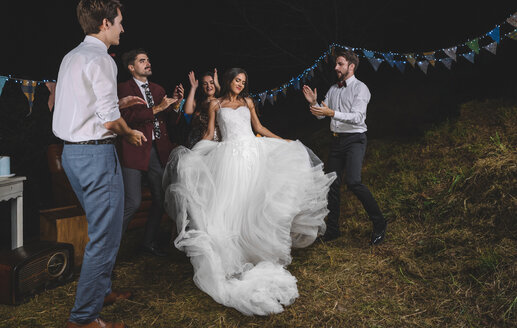 Glückliche Braut, die tanzt und Spaß hat, während ihre Freunde auf einer nächtlichen Feldparty klatschen - DAPF00946