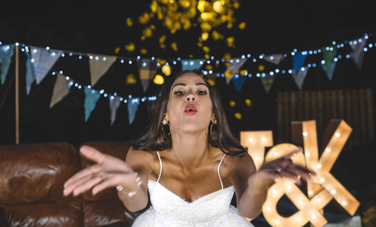 Porträt einer glücklichen Braut, die auf einer Nachtparty im Freien Konfetti ausbläst - DAPF00953