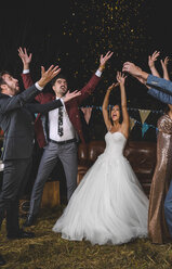 Cheerful wedding couple and friends raising their arms while confetti falling over their heads on a night party outdoors - DAPF00955