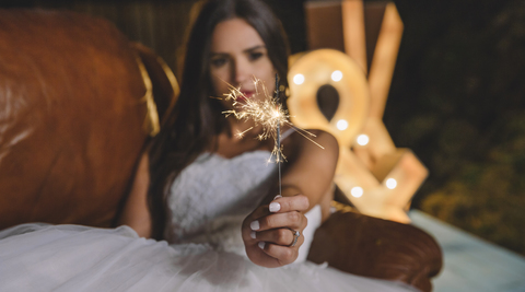 Nahaufnahme einer Wunderkerze in der Hand einer auf dem Sofa liegenden Braut auf einer Party im Freien, lizenzfreies Stockfoto