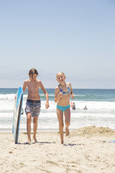 Junge mit Surfbrett und Mädchen spazieren am Strand in San Diego - FOLF05548