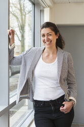 Businesswoman standing at window and smiling - FOLF05623