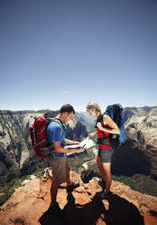 Hikers checking map at mountain cliff against clear sky - CAVF31182