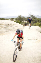 Couple riding bicycles on rocks against clear sky - CAVF31207